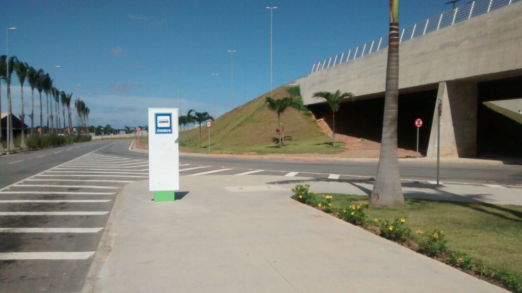 Parada de ônibus em frente ao Aeroporto Internacional de Natal, com calçada, faixa de pedestres e palmeiras