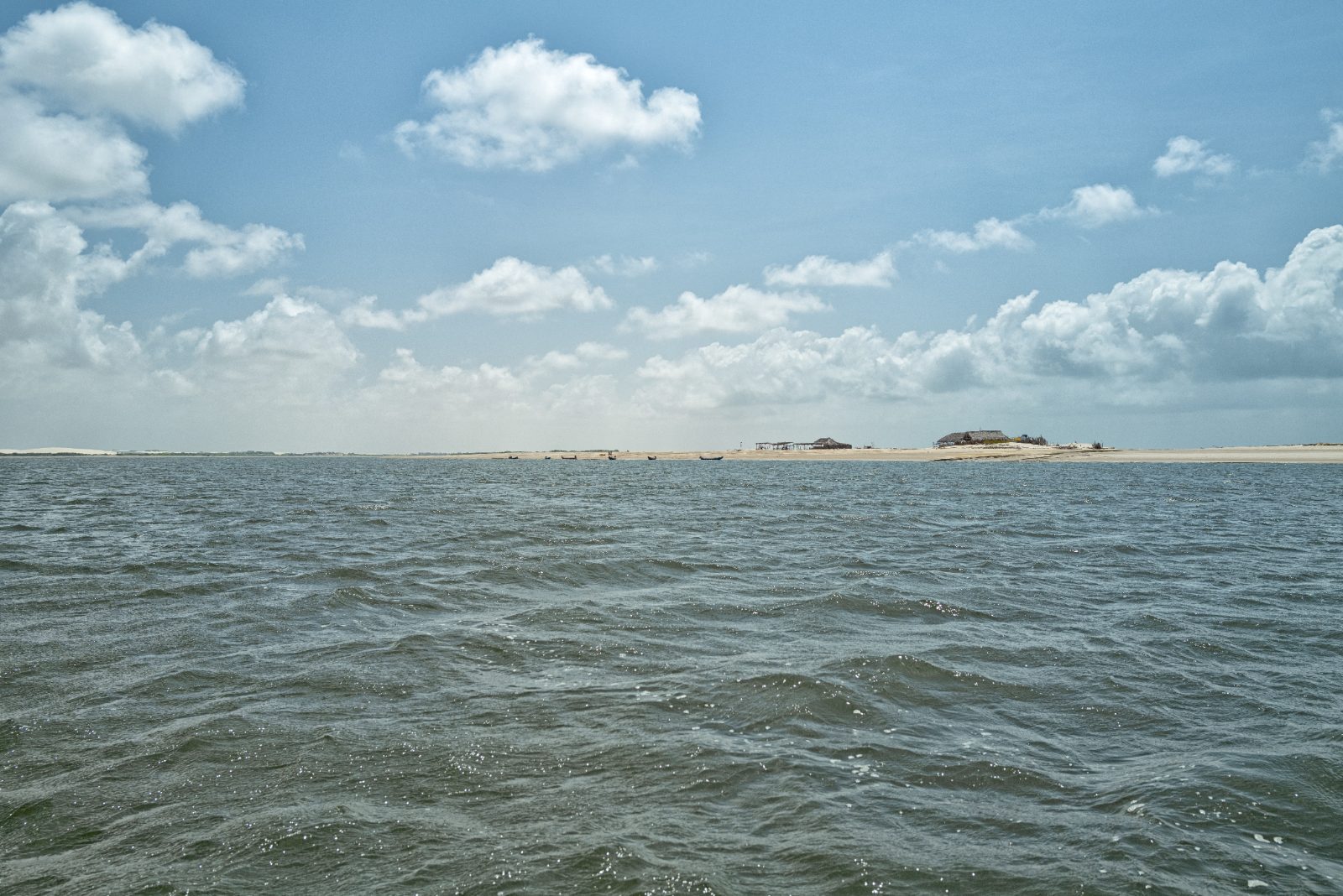 Águas da foz do Rio Preguiças e bancos de areia em Atins, sob céu azul com nuvens