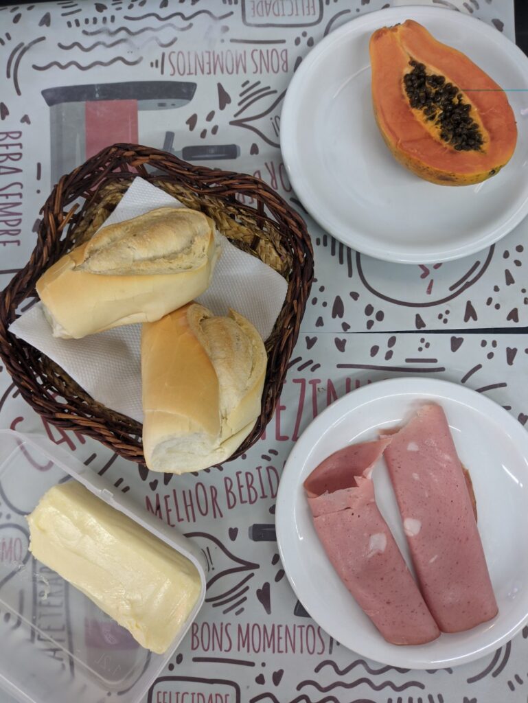 Café da manhã simples com pão francês, manteiga, frios e mamão