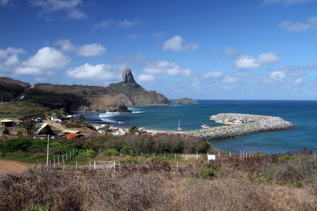 Porto de Santo Antônio em Fernando de Noronha com barcos, quebra-mar e o Morro do Pico ao fundo
