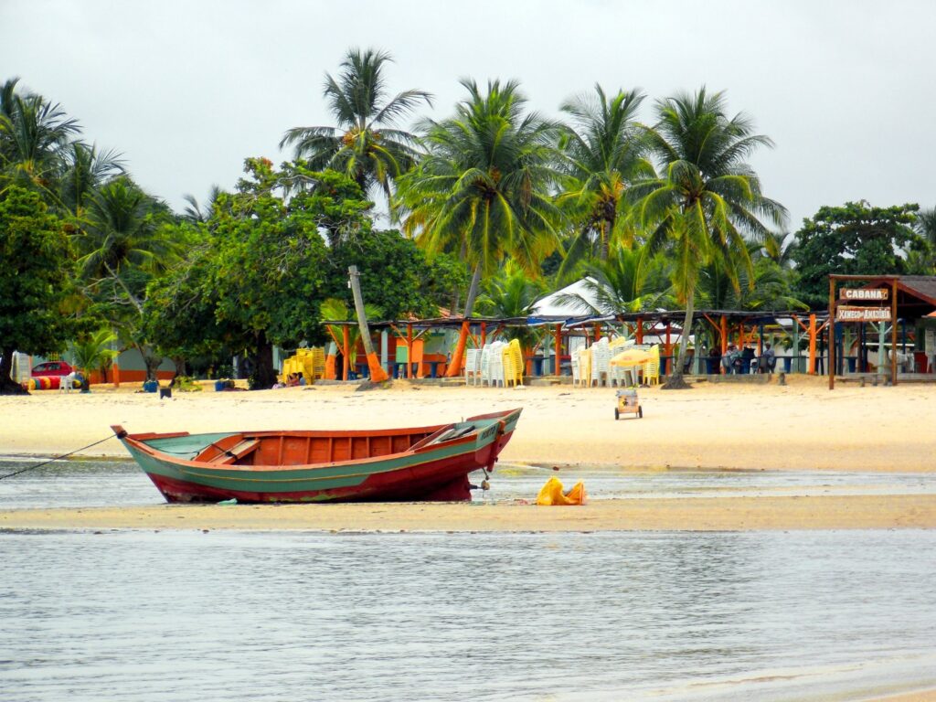 Barco de pesca na areia da Praia de Coroa Vermelha com barracas e coqueiros ao fundo