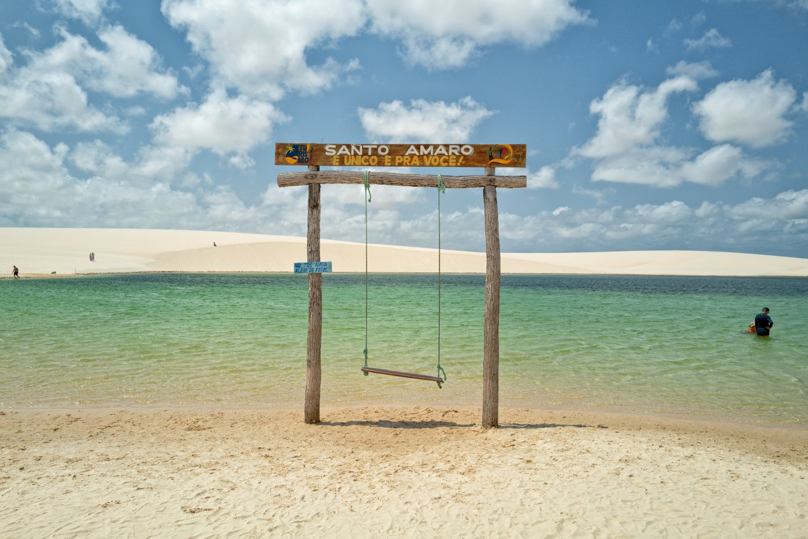 Balanço com placa de Santo Amaro à beira de uma lagoa de água verde entre as dunas dos Lençóis Maranhenses