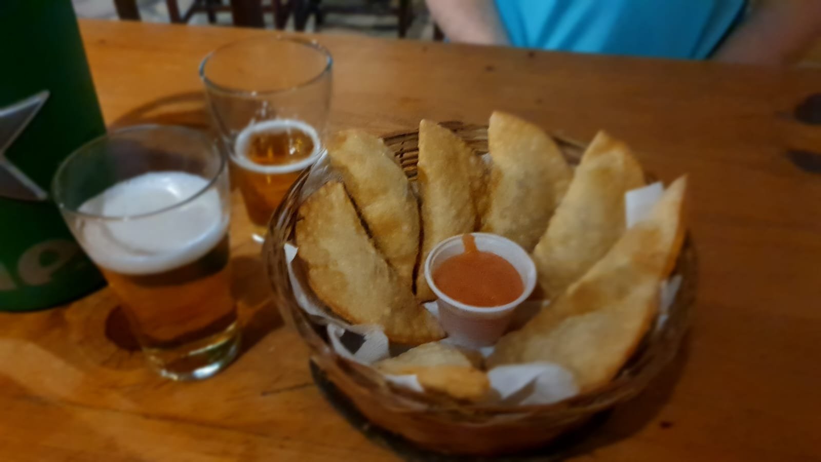 Cesta de pastéis de caranguejo com molho e copos de cerveja sobre mesa de madeira