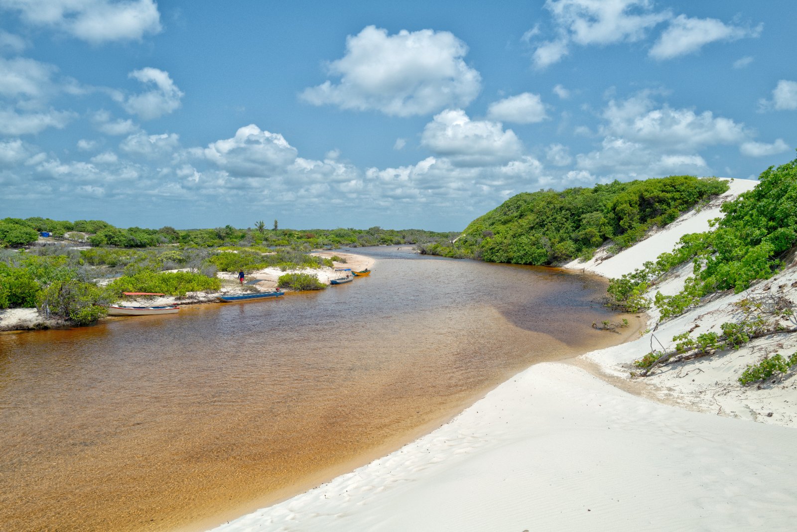 Rio de água escura entre dunas brancas e vegetação verde em Santo Amaro do Maranhão