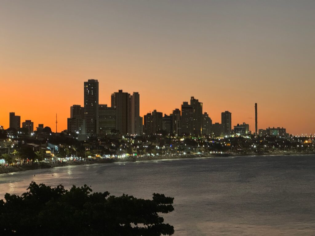 Orla de Ponta Negra ao entardecer, com prédios iluminados e o mar calmo