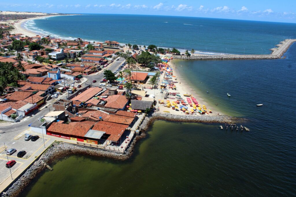 Vista aérea da praia da Redinha, com casas de telhado vermelho, barracas coloridas na areia e o rio Potengi