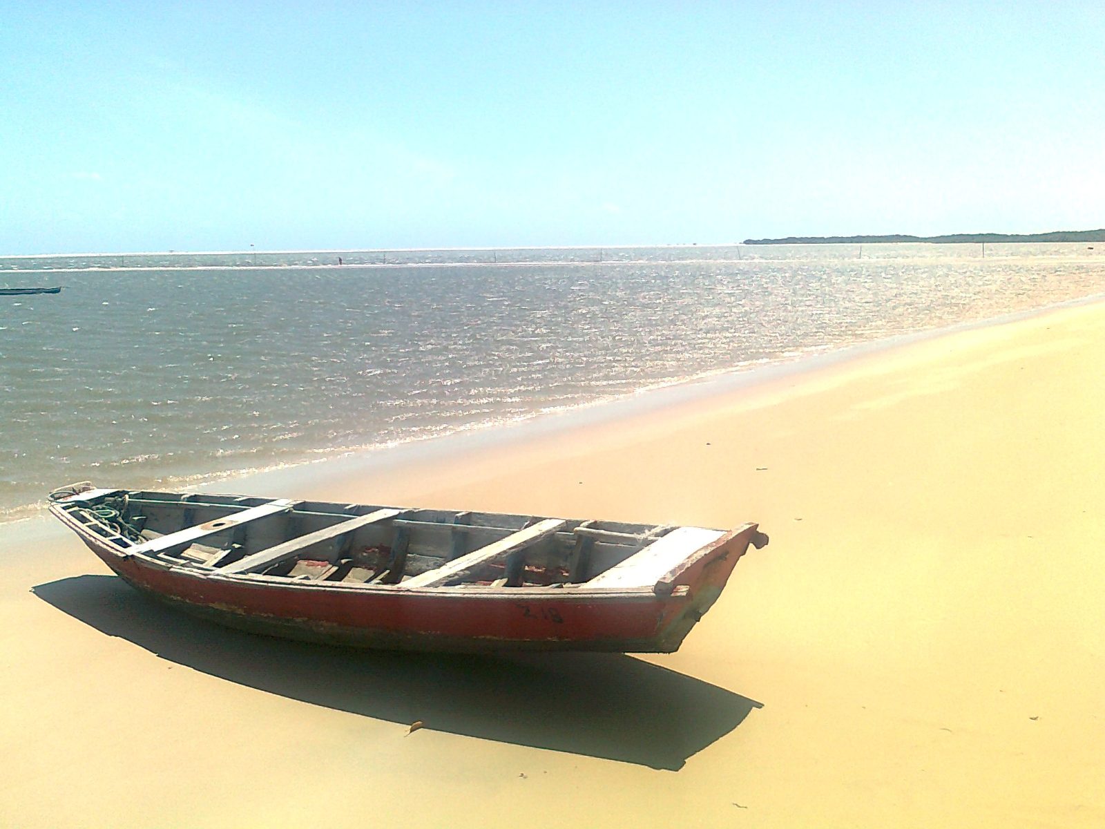 Barco de pesca na areia da praia de Atins, com o mar calmo ao fundo