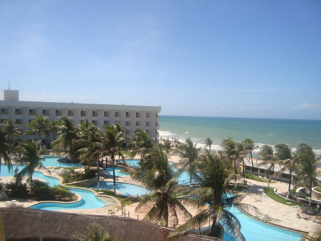 Área de piscinas e coqueiros de um hotel de frente para o mar na Via Costeira