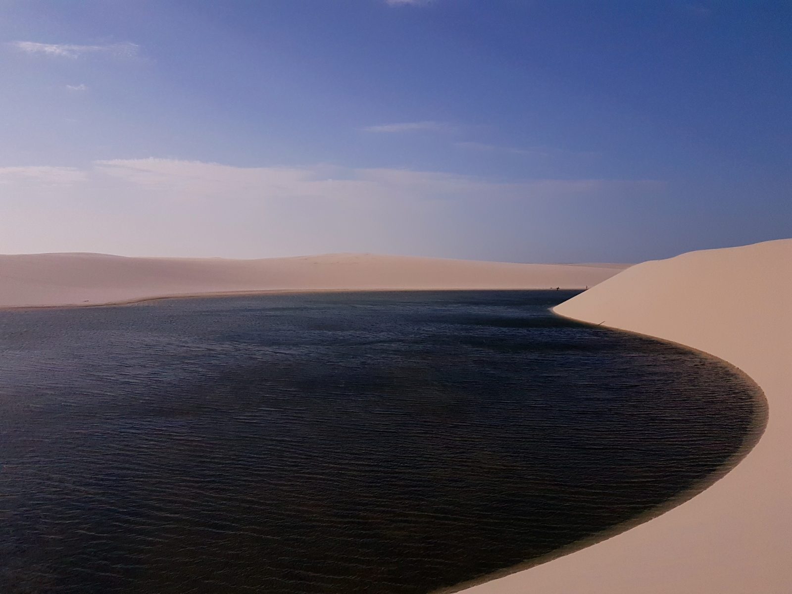 Lagoa escura cercada por dunas nos Lençóis Maranhenses em passeio saindo de Atins