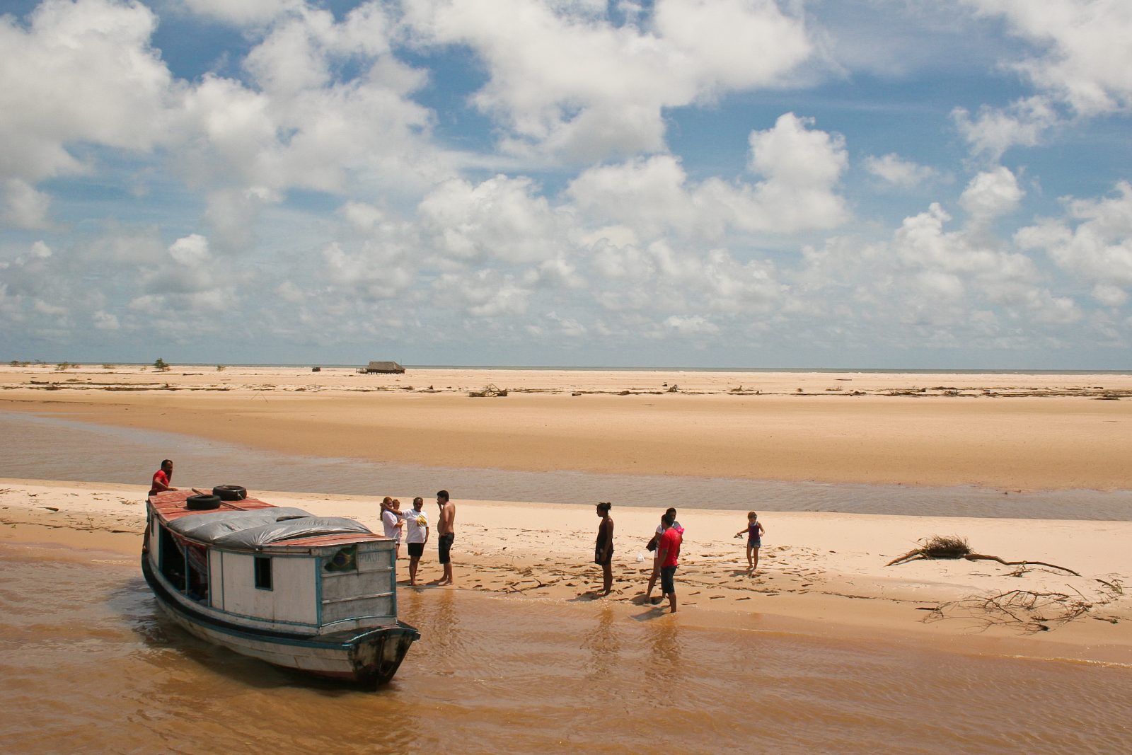 Barco parado na praia de uma ilha do Delta do Parnaíba com turistas na areia