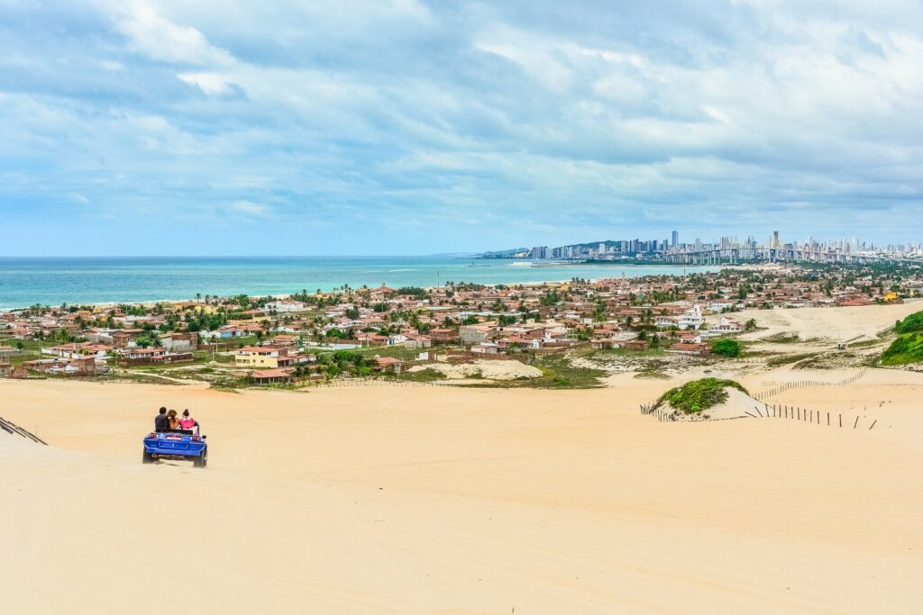 Buggy nas dunas de Genipabu, com casas da praia e os prédios de Natal ao fundo