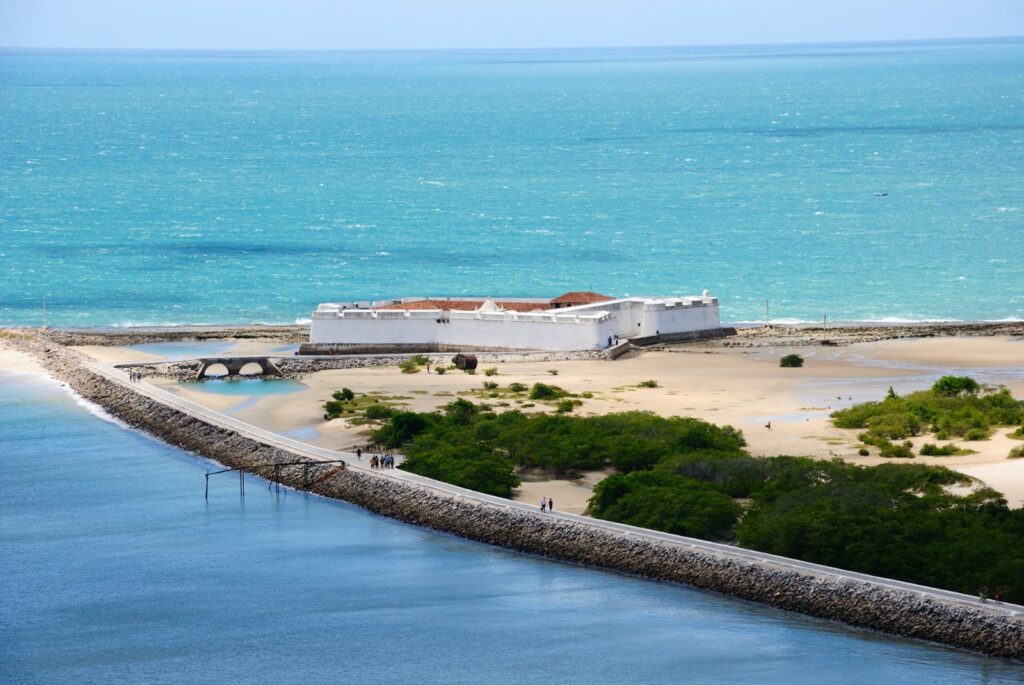 Forte dos Reis Magos, construção branca em forma de estrela no encontro do rio Potengi com o mar, com o caminho de pedras que leva até ele