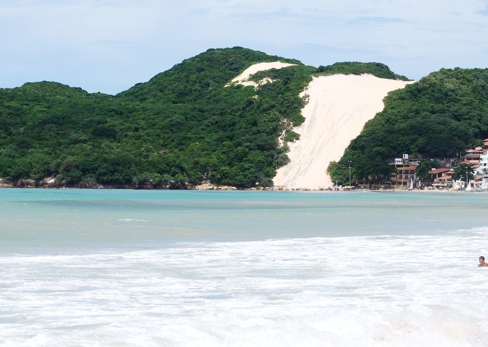 Morro do Careca, duna de areia clara cercada de vegetação, visto da praia de Ponta Negra