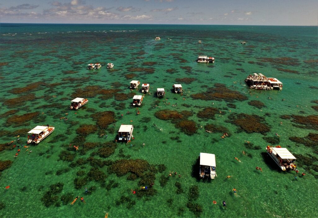 Vista aérea dos parrachos de Maracajaú, com recifes escuros sob o mar verde e barcos ancorados