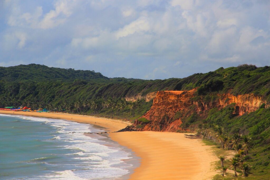 Baía dos Golfinhos, em Pipa, com areia dourada ao pé de falésias avermelhadas e vegetação