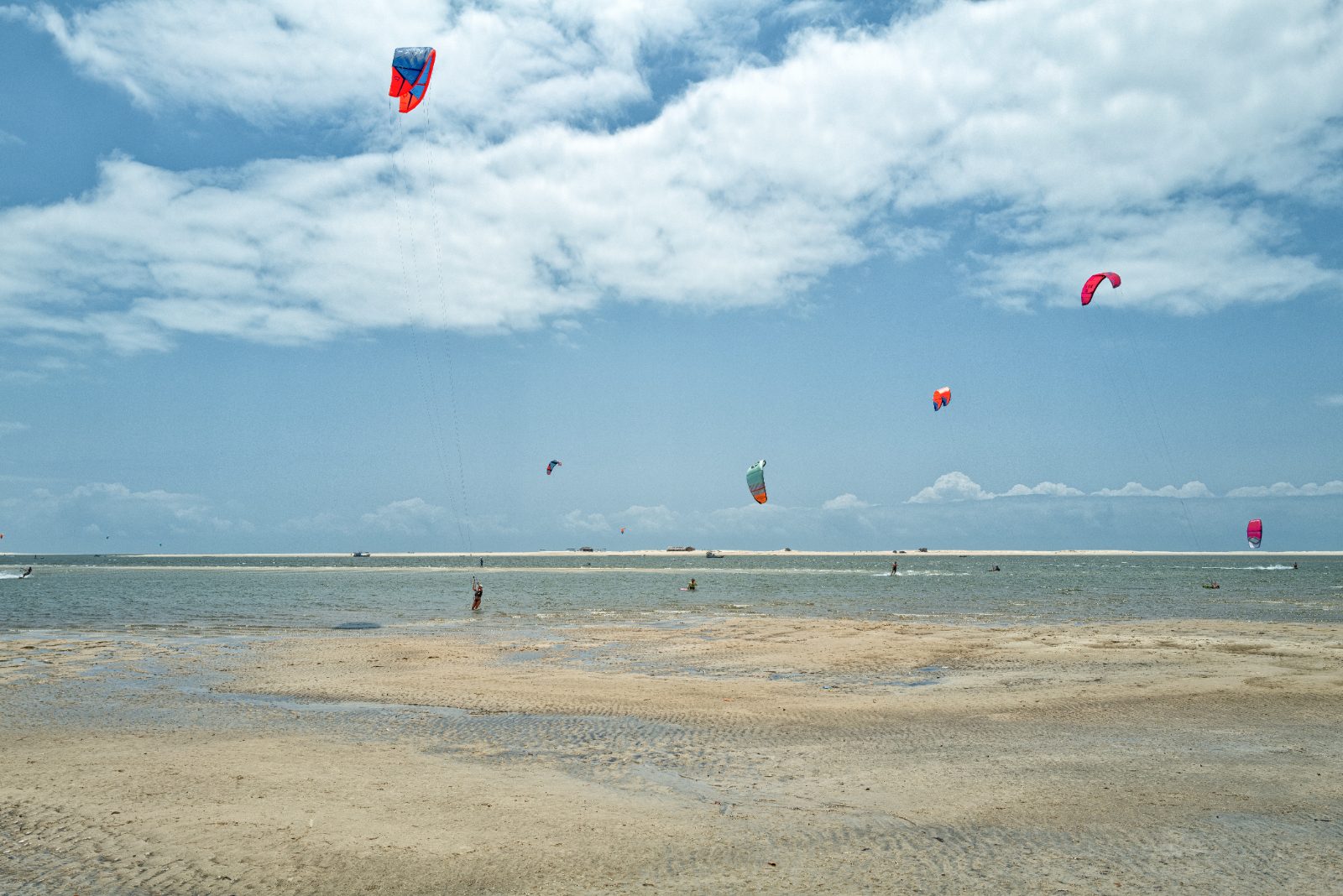 Kitesurfistas e velas coloridas no céu sobre a praia de Atins na maré baixa