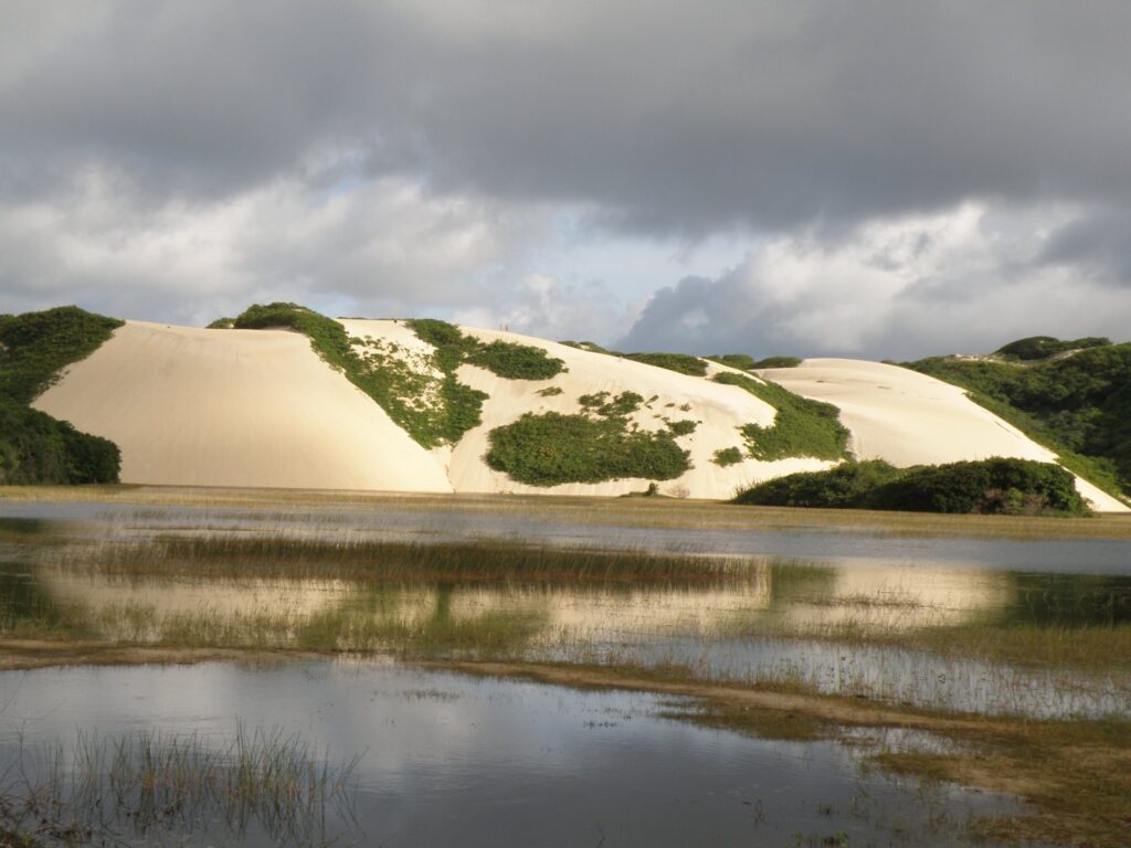 Dunas claras de Genipabu sob céu nublado, refletidas numa lagoa formada pela água da chuva