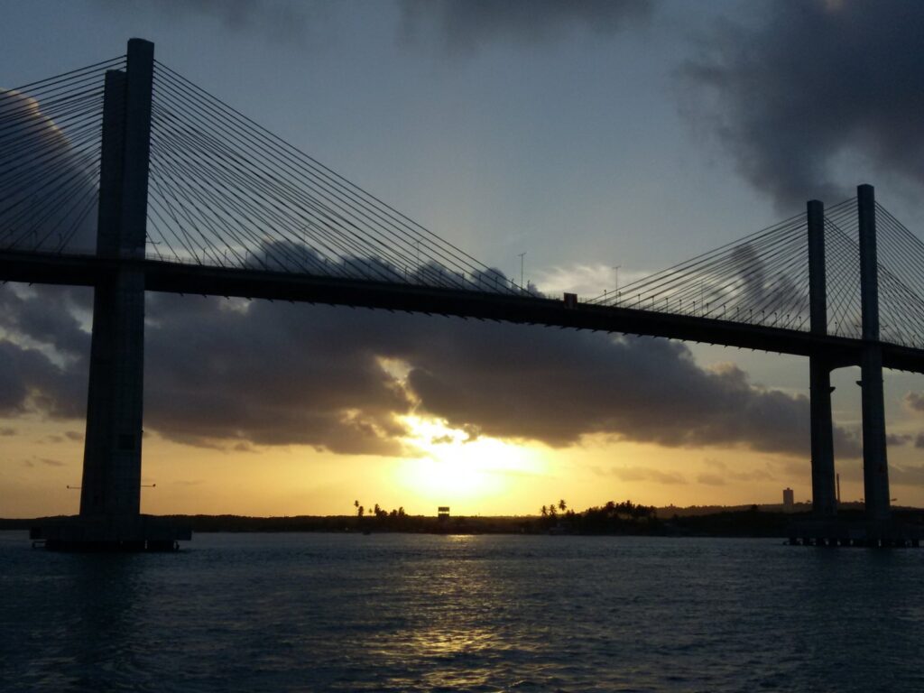 Silhueta da Ponte Newton Navarro sobre o rio Potengi ao pôr do sol, com nuvens douradas