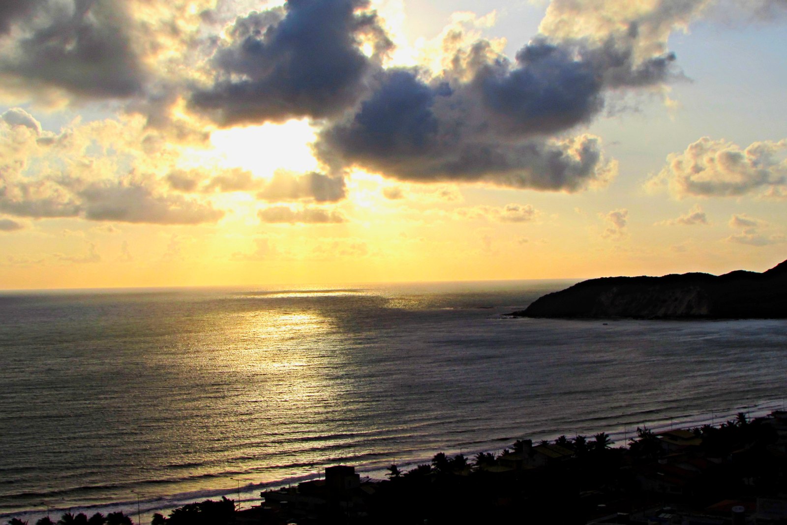 Pôr do sol sobre o mar de Ponta Negra, em Natal, com nuvens e o sol refletido na água