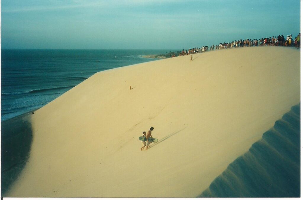 Duna do Pôr do Sol vista de cima, com pessoas no alto da crista e o mar ao lado, em Jericoacoara
