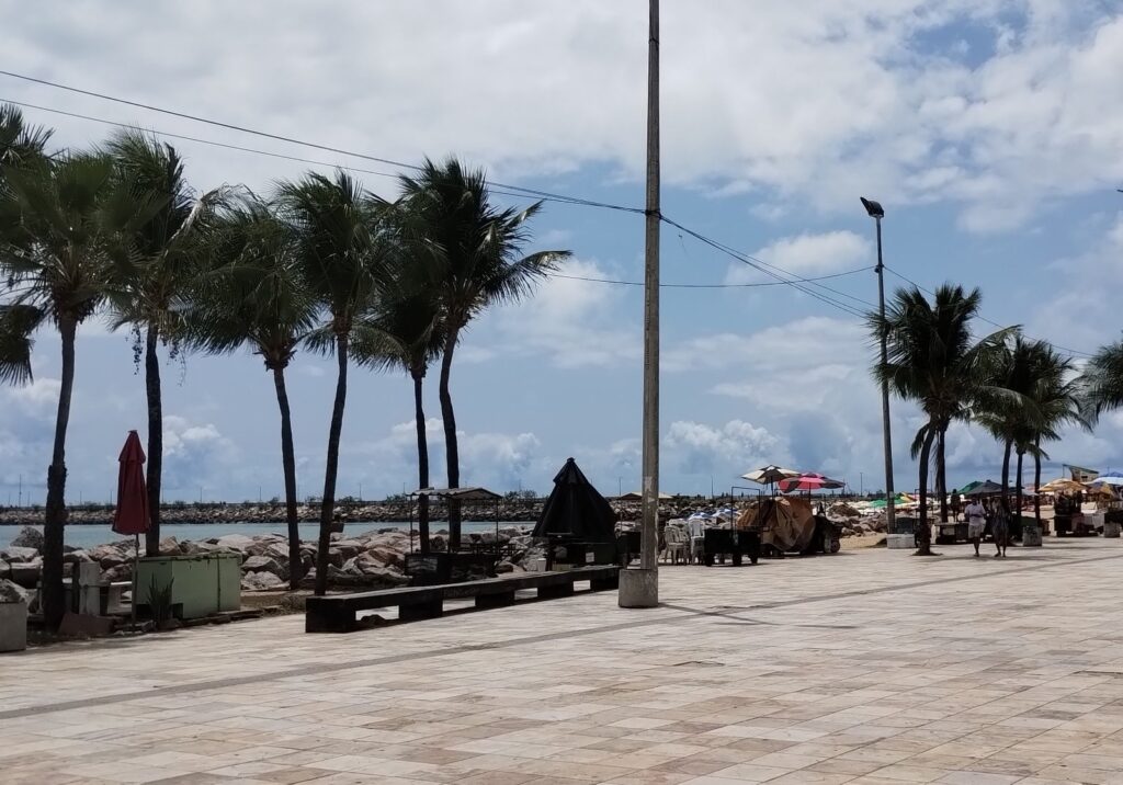 Praia de Iracema vista do calçadão, com banhistas no mar verde e a Ponte dos Ingleses ao fundo, em Fortaleza