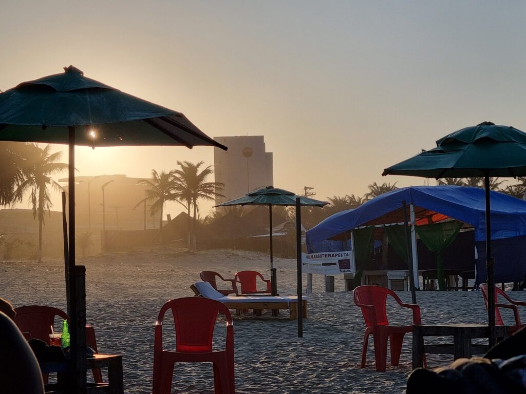 Mesas, cadeiras vermelhas e guarda-sóis de uma barraca na areia da Praia do Futuro ao pôr do sol, em Fortaleza
