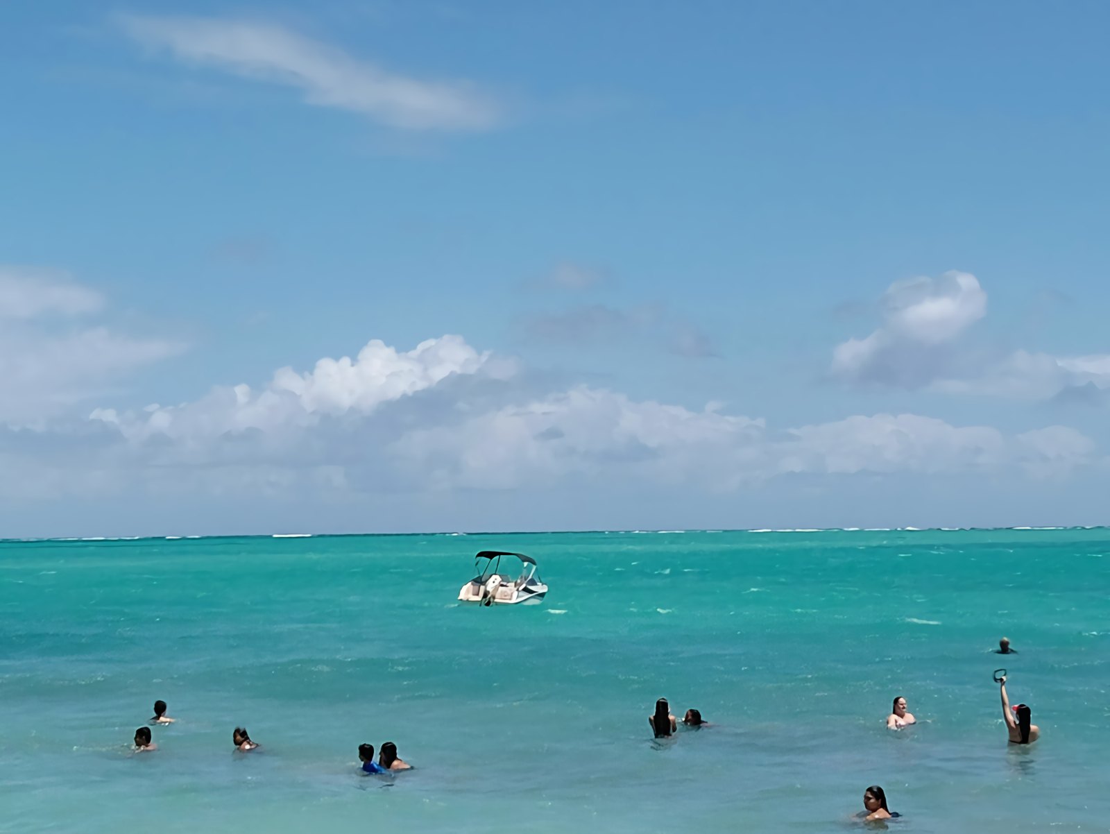 Banhistas nas piscinas naturais das galés de Maragogi, com água verde-turquesa e uma lancha ao fundo