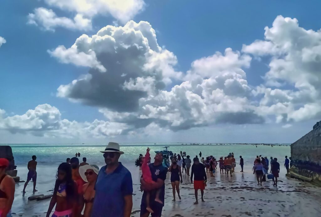 Grupo de turistas caminhando na água rasa das piscinas naturais de Maragogi durante a maré baixa