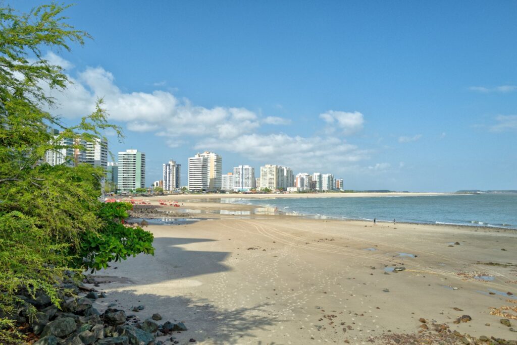 Praia da Ponta d'Areia em dia de sol, com areia clara, mar calmo e prédios ao fundo