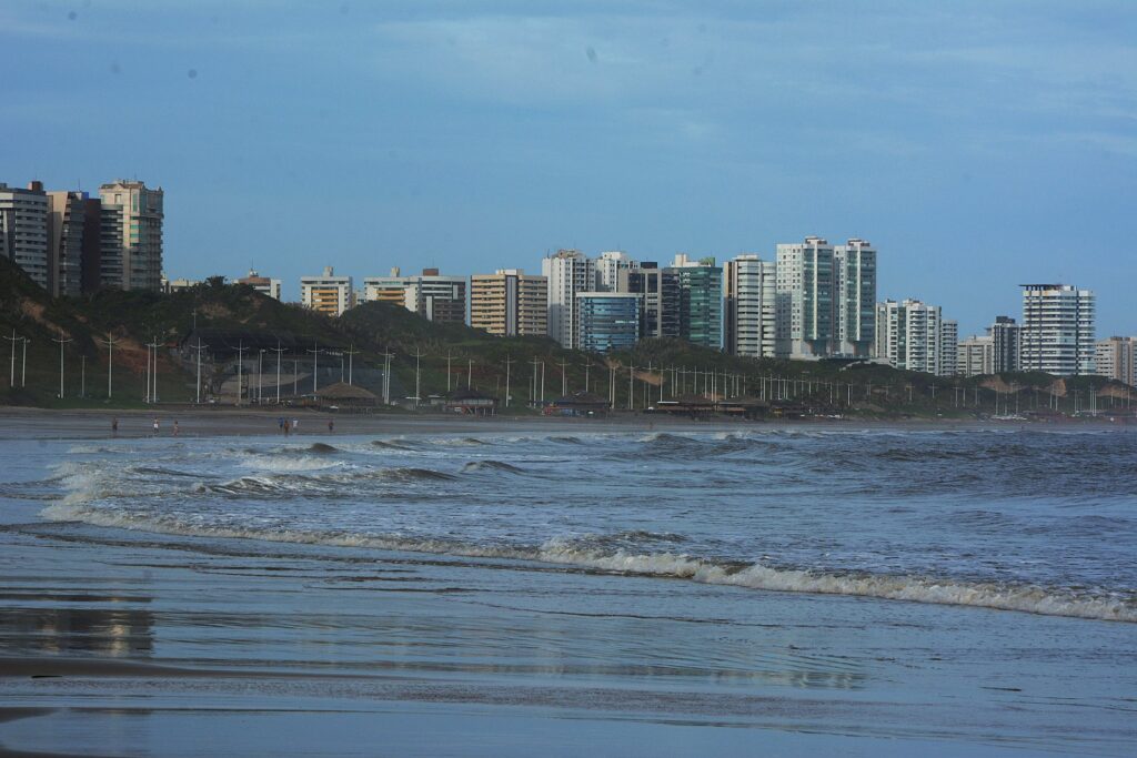Faixa de areia molhada da Praia do Calhau com prédios da orla de São Luís ao fundo
