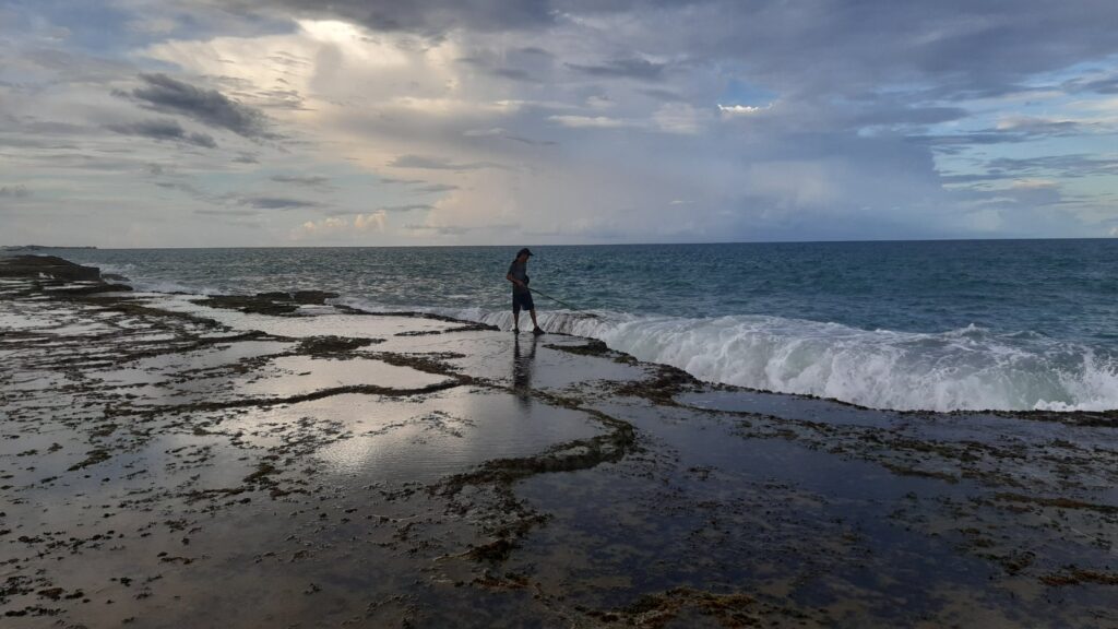 Pessoa caminhando sobre os recifes da Praia do Meio, em Natal, com céu nublado no fim de tarde