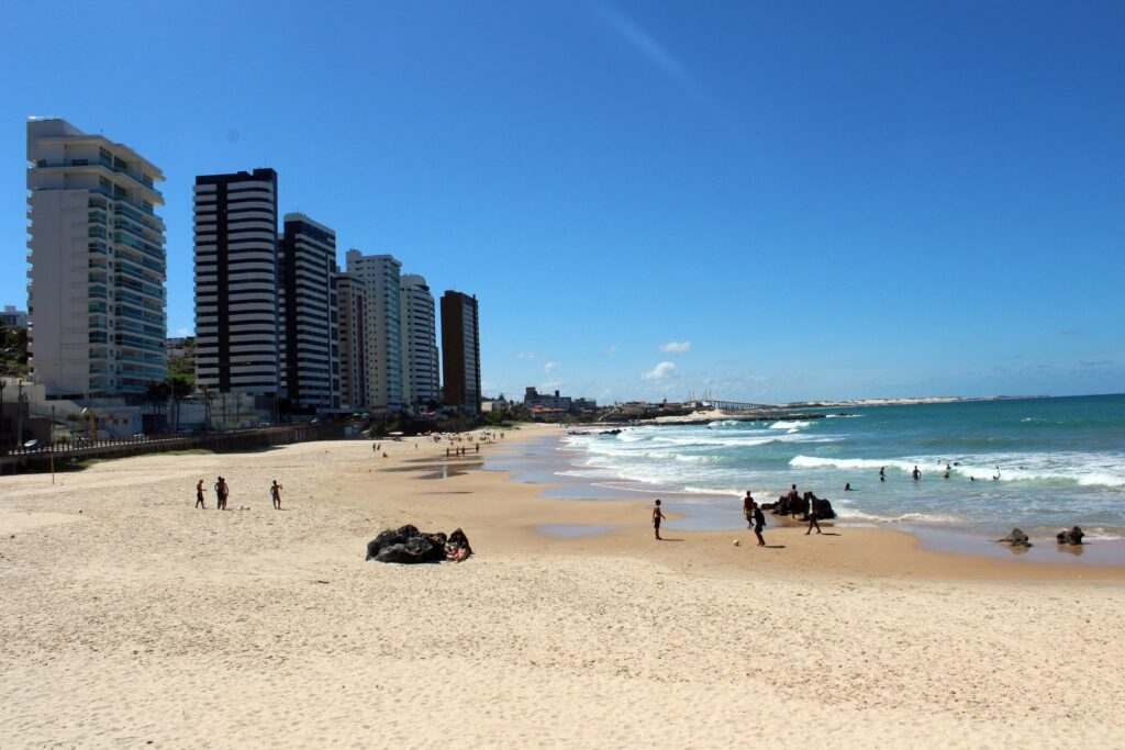 Faixa de areia da Praia dos Artistas com prédios à beira-mar e céu azul em Natal