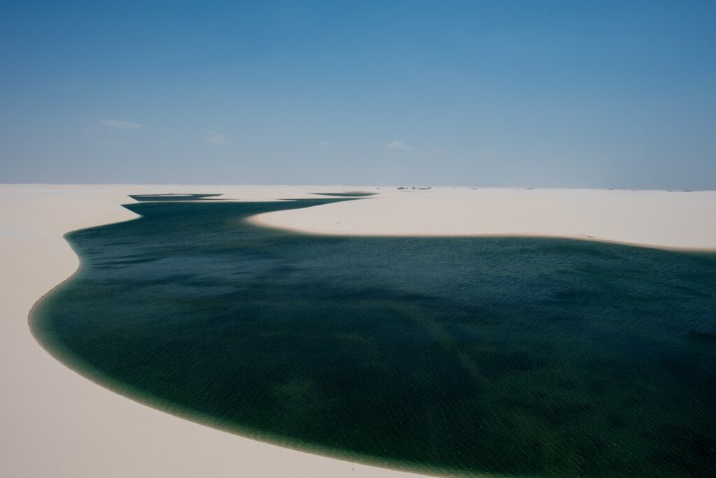 Lagoa de água verde-escura entre dunas brancas nos Lençóis Maranhenses