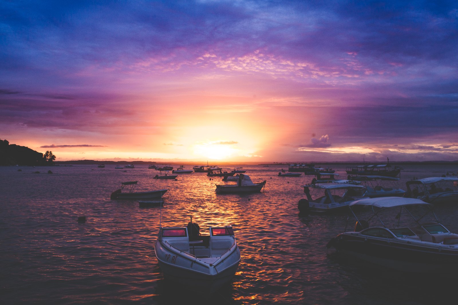 Barcos ancorados no mar de Morro de São Paulo ao pôr do sol, com céu lilás e laranja