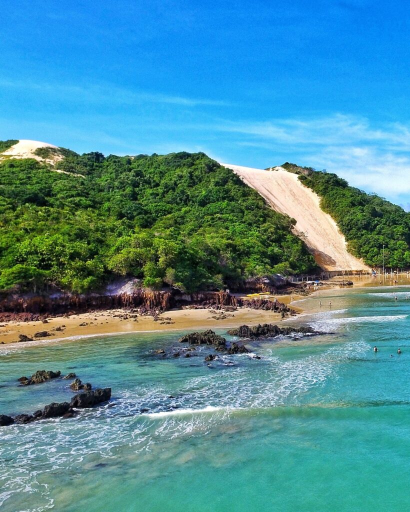 Morro do Careca, duna de areia clara cercada de vegetação verde, no fim da praia de Ponta Negra, em Natal