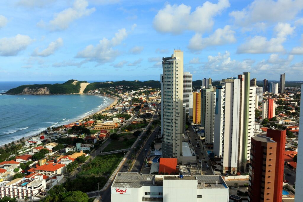 Vista aérea da praia de Ponta Negra, em Natal, com prédios à beira-mar e o Morro do Careca ao fundo