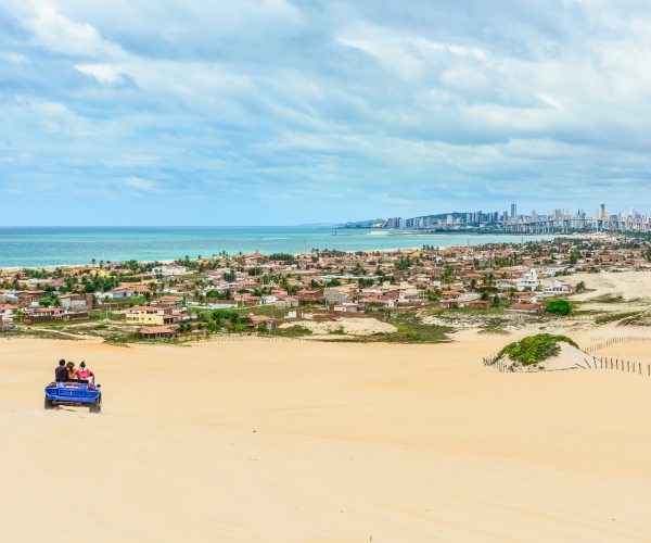 Buggy nas dunas de Genipabu, com casas da praia e os prédios de Natal ao fundo