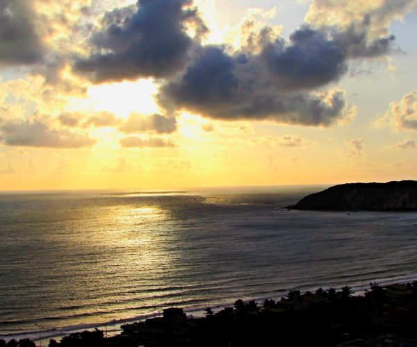 Pôr do sol sobre o mar de Ponta Negra, em Natal, com nuvens e o sol refletido na água