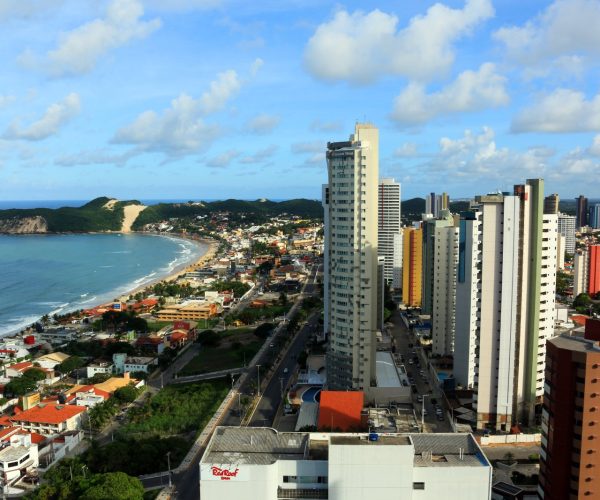 Vista aérea da praia de Ponta Negra, em Natal, com prédios à beira-mar e o Morro do Careca ao fundo